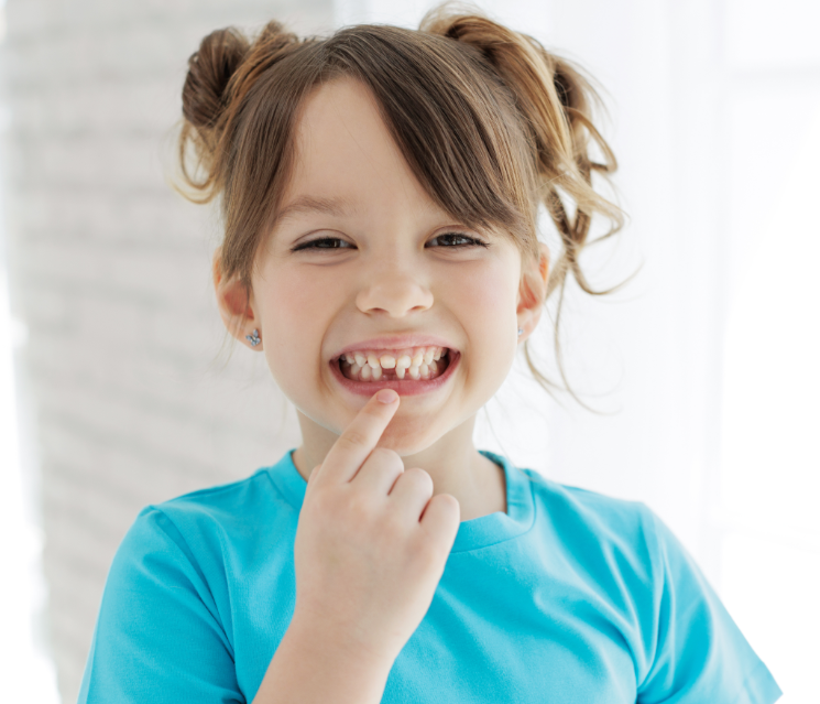Little girl in blue shirt pointing at missing tooth