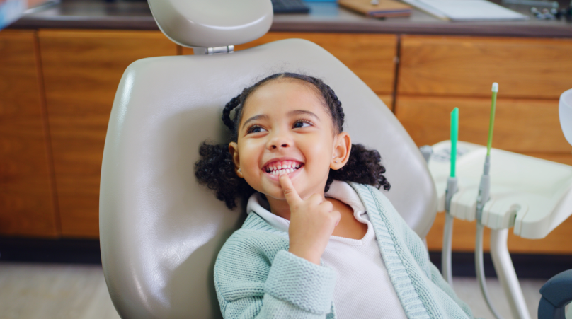Child in dental chair pointing to mouth